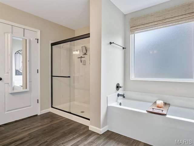 full bath featuring wood finished floors, a stall shower, a bath, and baseboards