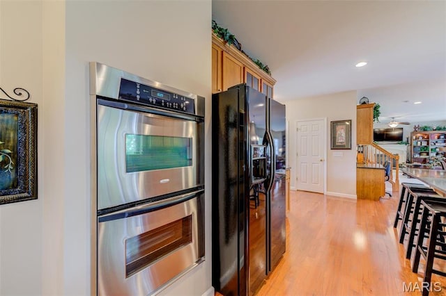 41 Deer Creek Dr, Ofallon, MO 63366 - kitchen with black fridge with ice dispenser, stainless steel double oven, light wood-type flooring, brown cabinetry, and recessed lighting