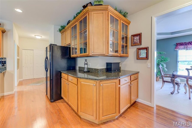 41 Deer Creek Dr, Ofallon, MO 63366 - kitchen featuring freestanding refrigerator, light wood finished floors, glass insert cabinets, baseboards, and dark stone countertops