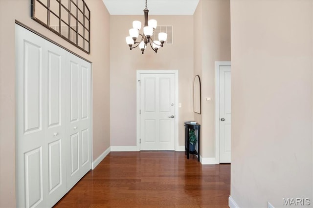 entryway with a chandelier, wood finished floors, a towering ceiling, and baseboards