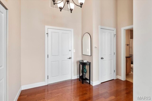 foyer with a towering ceiling, a chandelier, wood finished floors, and baseboards