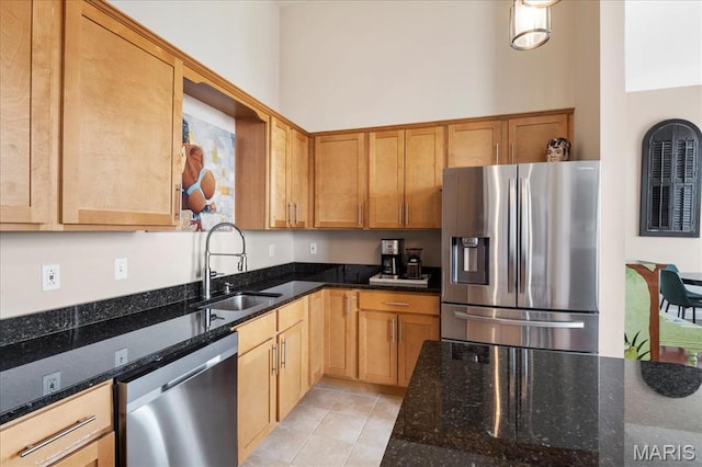 kitchen featuring stainless steel appliances, a sink, dark stone counters, and light tile patterned floors