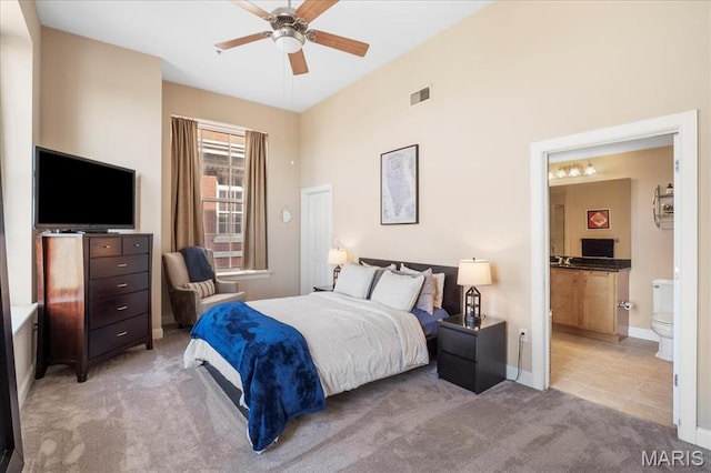 bedroom with light colored carpet, ensuite bathroom, baseboards, and ceiling fan