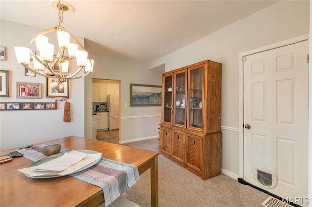 dining space with a chandelier, light colored carpet, and baseboards