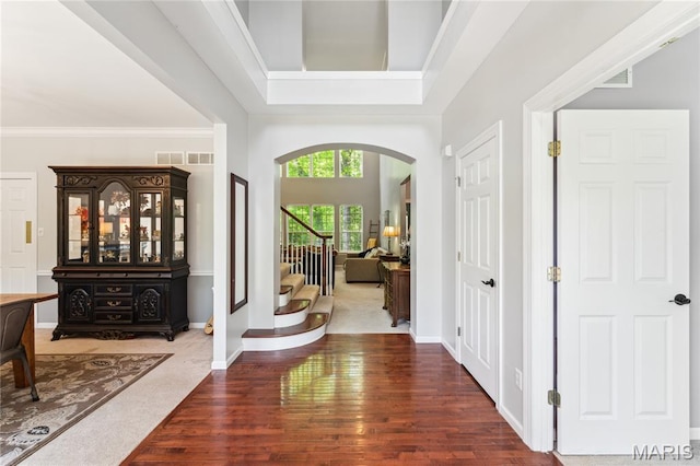 foyer featuring arched walkways, wood finished floors, stairway, crown molding, and baseboards