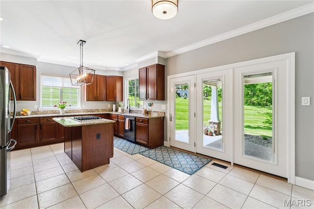 kitchen featuring appliances with stainless steel finishes, a sink, ornamental molding, a kitchen island, and light stone counters