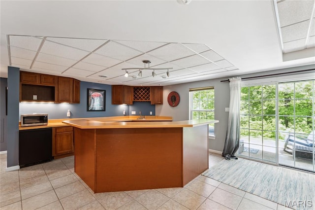 kitchen with light tile patterned floors, a center island, stainless steel microwave, and light countertops