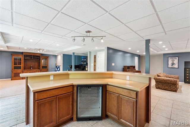 kitchen featuring wine cooler, open floor plan, light countertops, brown cabinetry, and light tile patterned floors
