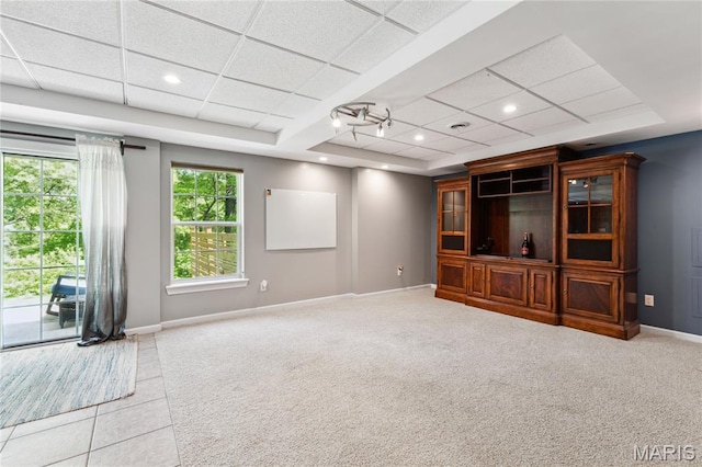 unfurnished living room featuring a tray ceiling, baseboards, carpet, a paneled ceiling, and tile patterned flooring