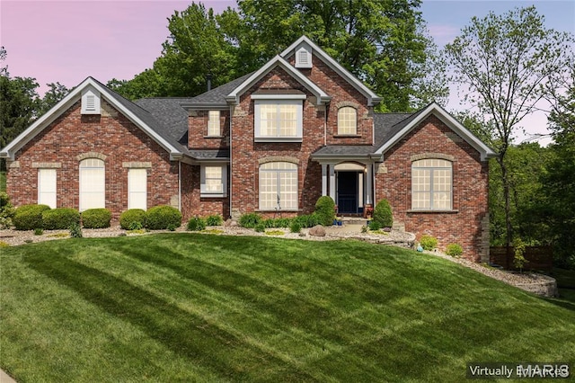 view of front of home with a front lawn, brick siding, and roof with shingles