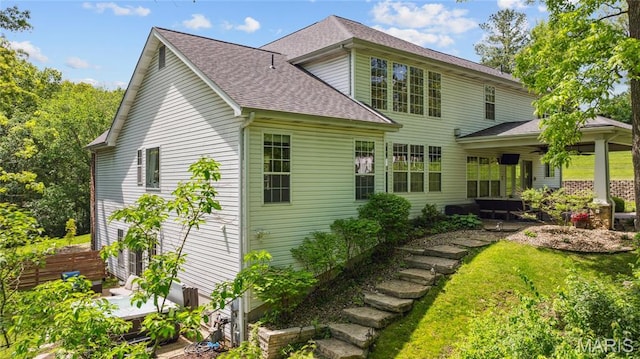 back of property with a shingled roof and a lawn