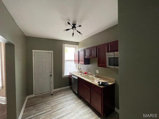 kitchen with appliances with stainless steel finishes, a sink, light wood finished floors, baseboards, and light countertops