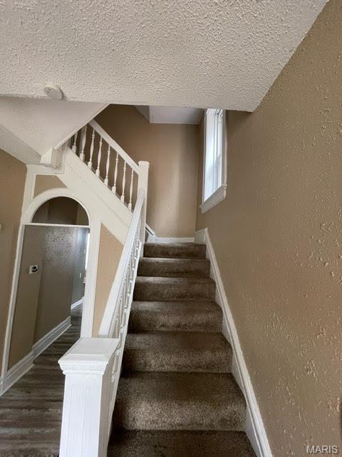 stairs featuring a textured ceiling, wood finished floors, baseboards, and a textured wall