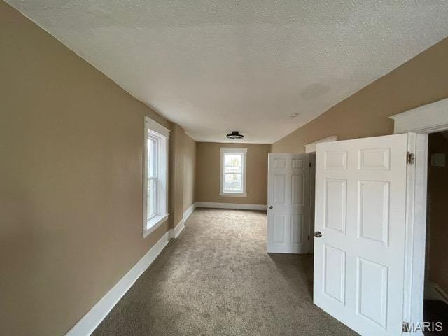 empty room with carpet floors, baseboards, a textured ceiling, and lofted ceiling