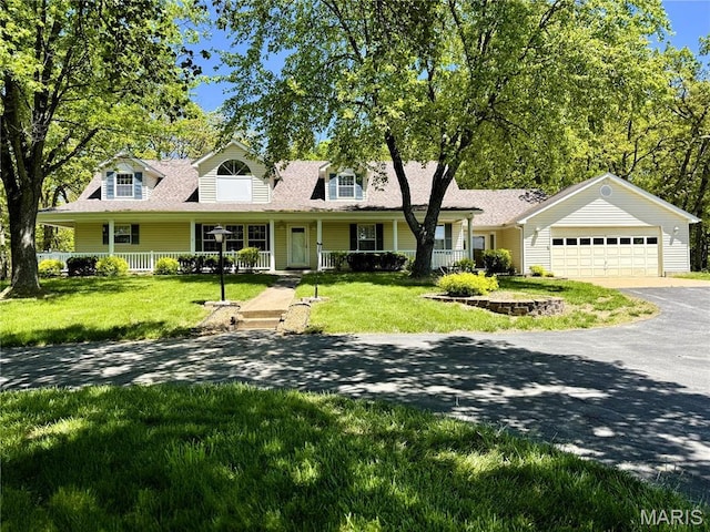 new england style home featuring a porch, driveway, a garage, and a front yard