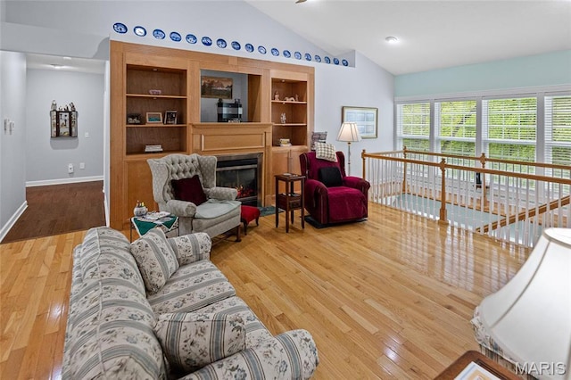 living area featuring lofted ceiling, wood finished floors, a glass covered fireplace, and baseboards