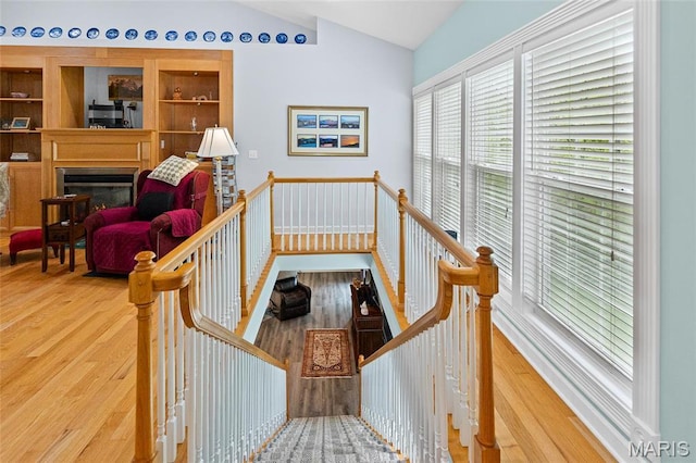 stairs featuring lofted ceiling, wood finished floors, and a glass covered fireplace