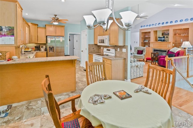 dining space featuring ceiling fan, a fireplace, vaulted ceiling, and a chandelier