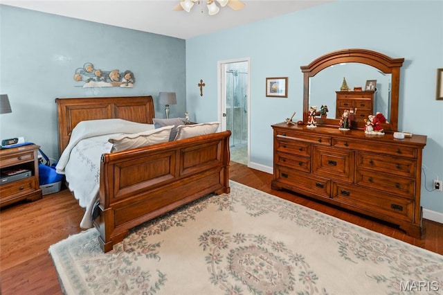 bedroom featuring wood finished floors, baseboards, a ceiling fan, and ensuite bath