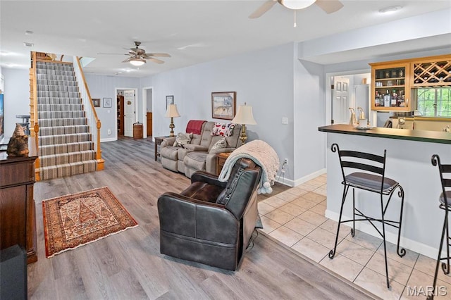 living room featuring ceiling fan, bar with sink, stairway, and baseboards