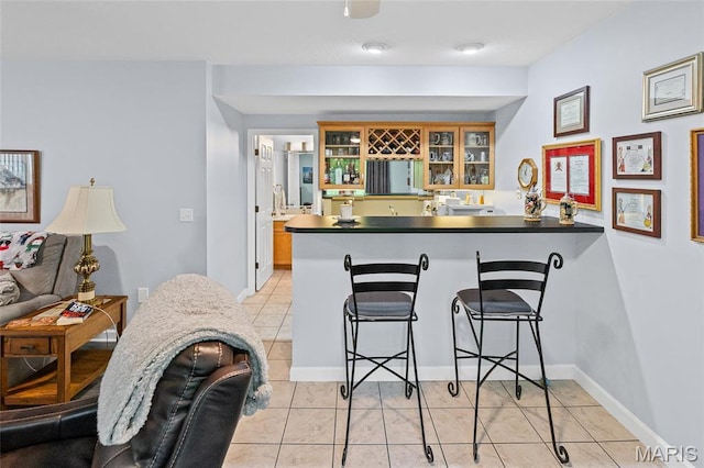 kitchen with a peninsula, dark countertops, a kitchen bar, glass insert cabinets, and light tile patterned flooring
