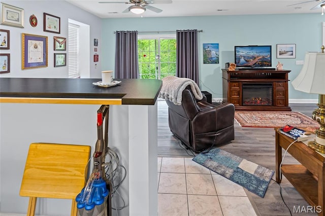 living room featuring ceiling fan, light wood-style floors, and a glass covered fireplace
