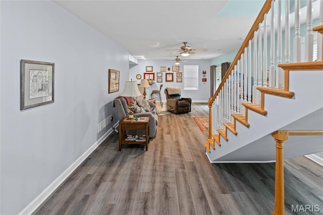 living area featuring wood finished floors, ceiling fan, baseboards, and stairway