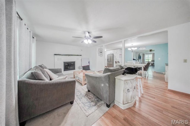 living area featuring light wood-type flooring, ceiling fan, and a brick fireplace