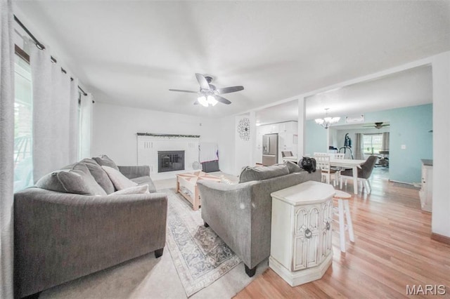 living area with light wood-style floors, a ceiling fan, and a fireplace