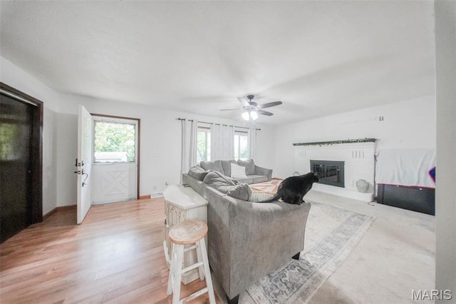 living room featuring a fireplace, ceiling fan, and light wood finished floors