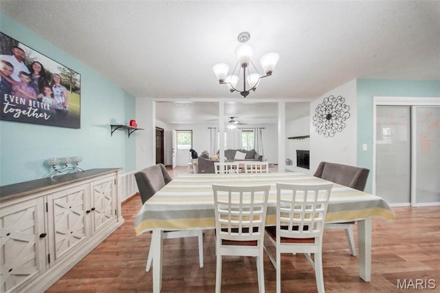 dining space featuring wood finished floors, a chandelier, a ceiling fan, and a fireplace