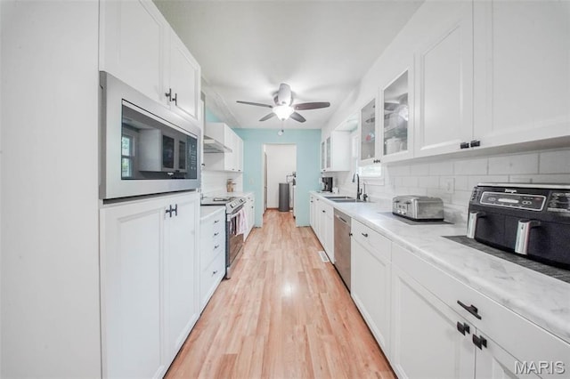 kitchen with appliances with stainless steel finishes, a sink, white cabinets, light countertops, and tasteful backsplash