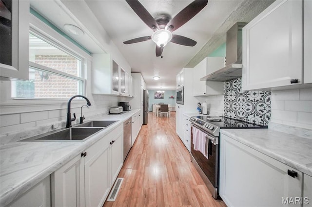 kitchen featuring stainless steel appliances, wall chimney range hood, a sink, and white cabinets