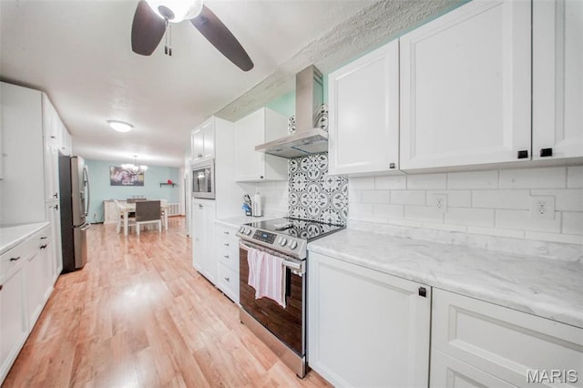 kitchen featuring stainless steel appliances, wall chimney exhaust hood, white cabinets, a ceiling fan, and light wood-type flooring