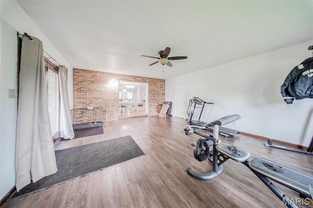 workout room featuring brick wall, a ceiling fan, wood finished floors, and baseboards