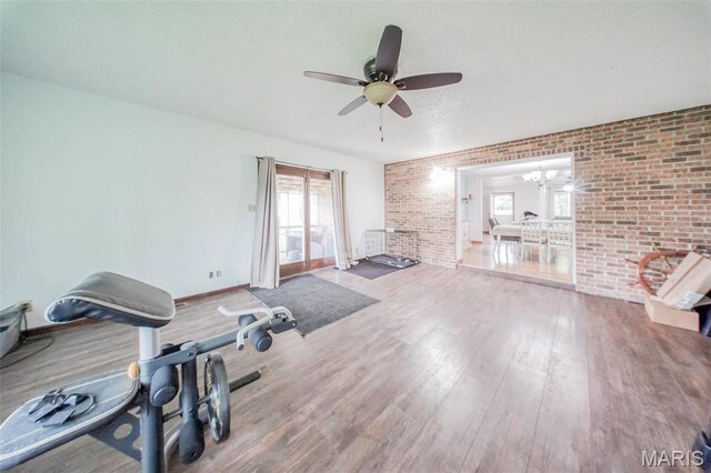 exercise area featuring wood finished floors, a ceiling fan, brick wall, baseboards, and a chandelier