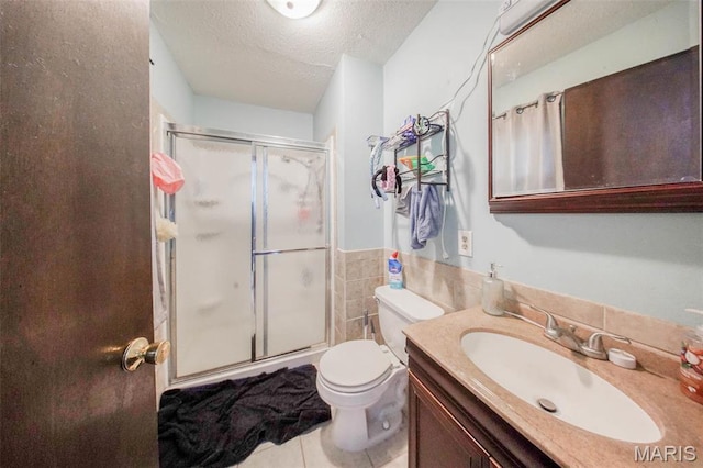 bathroom with a shower stall, a textured ceiling, tile patterned floors, vanity, and tile walls