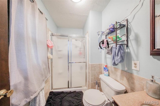 bathroom with a textured ceiling, a shower stall, tile walls, toilet, and vanity
