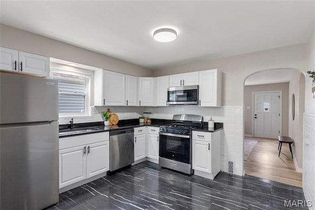 312 Waller Ave, Saint Louis, MO 63125 - kitchen featuring stainless steel appliances, a sink, dark countertops, arched walkways, and white cabinets