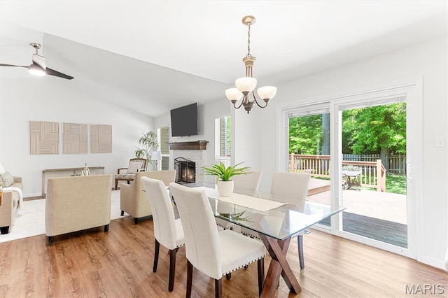 dining space featuring a lit fireplace, light wood-type flooring, lofted ceiling, a chandelier, and a ceiling fan