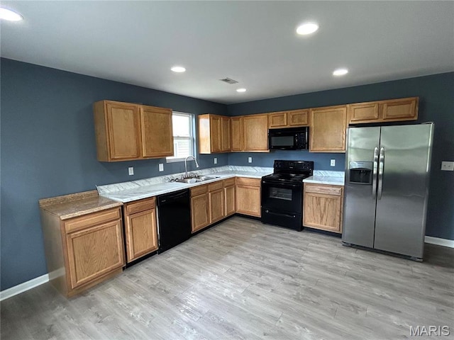 kitchen featuring black appliances, a sink, light countertops, light wood-type flooring, and baseboards