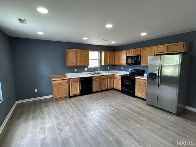 kitchen with black appliances, a sink, light countertops, light wood-type flooring, and recessed lighting