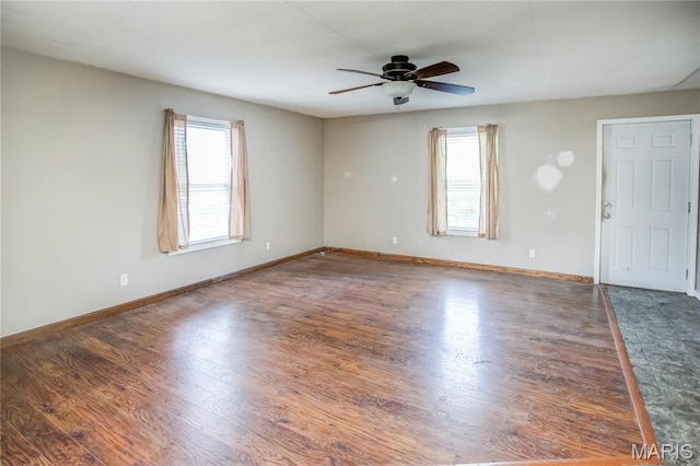 empty room with healthy amount of natural light, ceiling fan, wood finished floors, and baseboards
