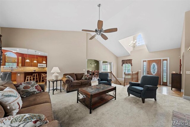living area with high vaulted ceiling, light carpet, ceiling fan, a chandelier, and arched walkways