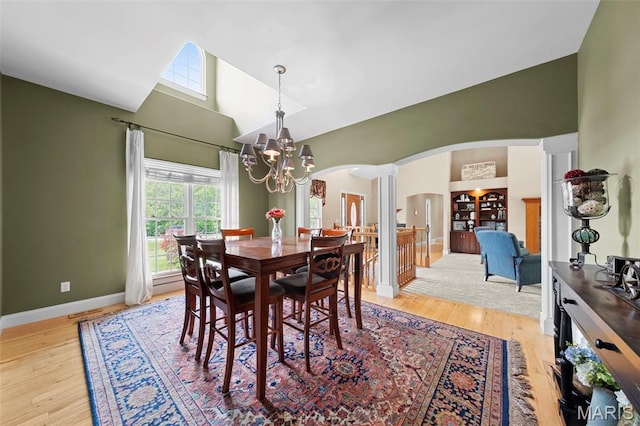 dining room featuring arched walkways, ornate columns, a chandelier, high vaulted ceiling, and light wood-style floors