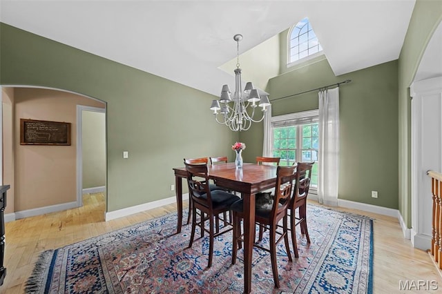 dining area featuring a chandelier, arched walkways, light wood-style flooring, baseboards, and high vaulted ceiling
