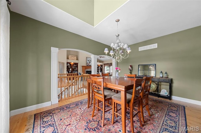 dining room with ornate columns, arched walkways, wood finished floors, baseboards, and high vaulted ceiling