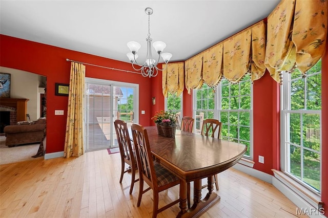 dining space featuring a chandelier, light wood-type flooring, a fireplace, and baseboards