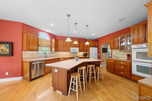 kitchen featuring white appliances, a sink, light wood finished floors, a kitchen bar, and light countertops