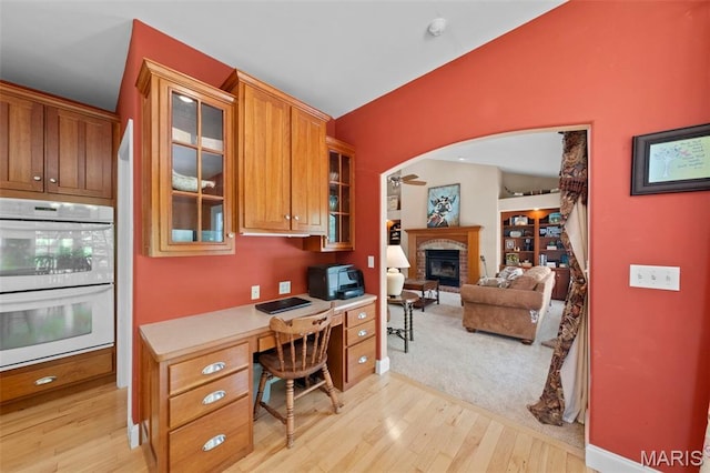 office space featuring a glass covered fireplace, light wood-style flooring, built in study area, arched walkways, and baseboards